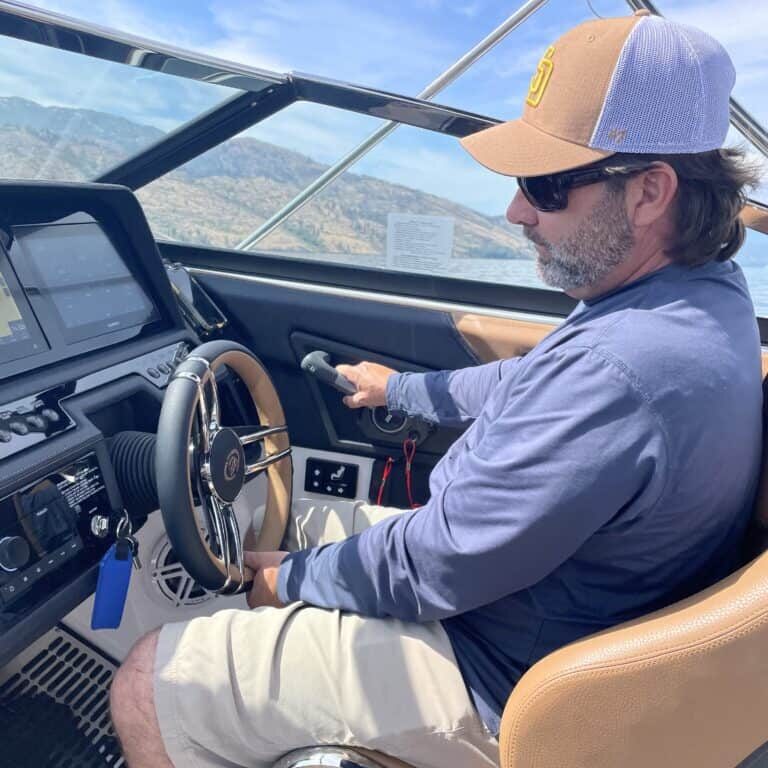 Man sitting at the helm of a powerboat, looking at dashboard controls